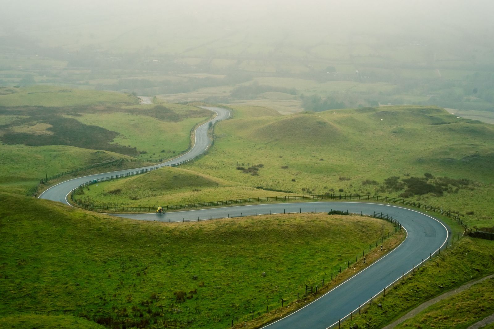 Estrada sinuosa atravessando colinas verdes sob névoa