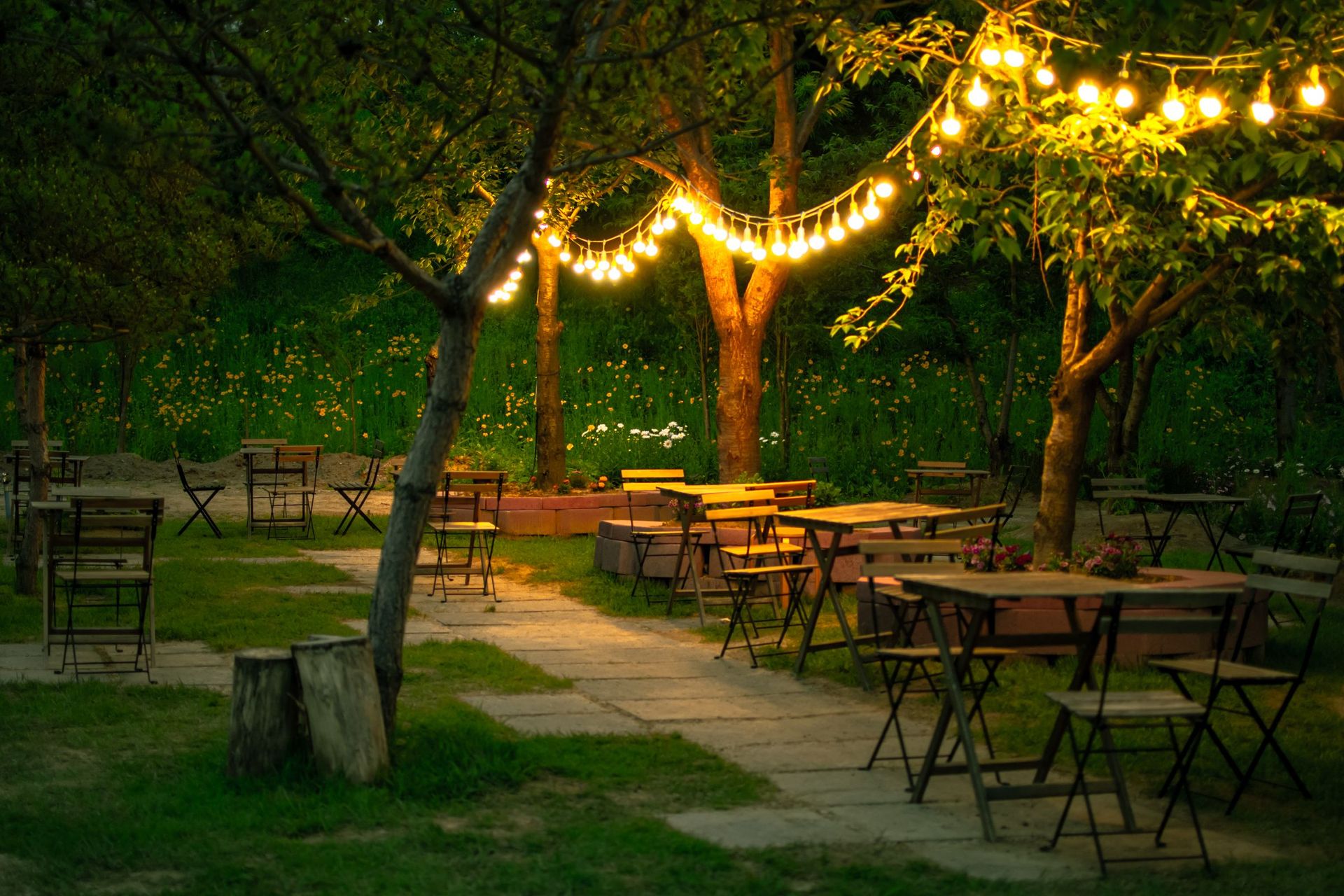 Jardim com mesas vazias e varal de lâmpadas acesas ao entardecer