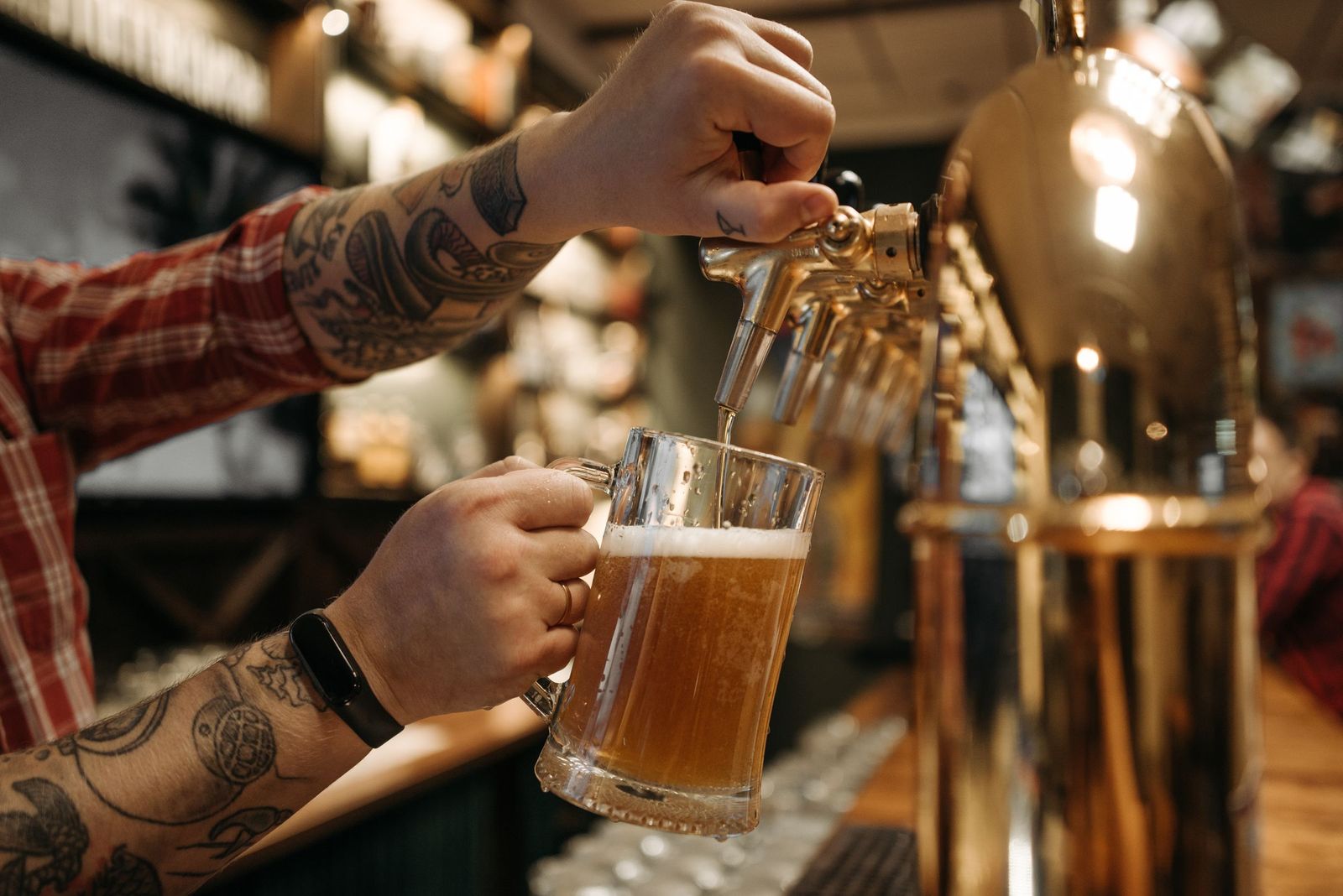 Mãos enchendo uma caneca de chope em uma torneira dourada