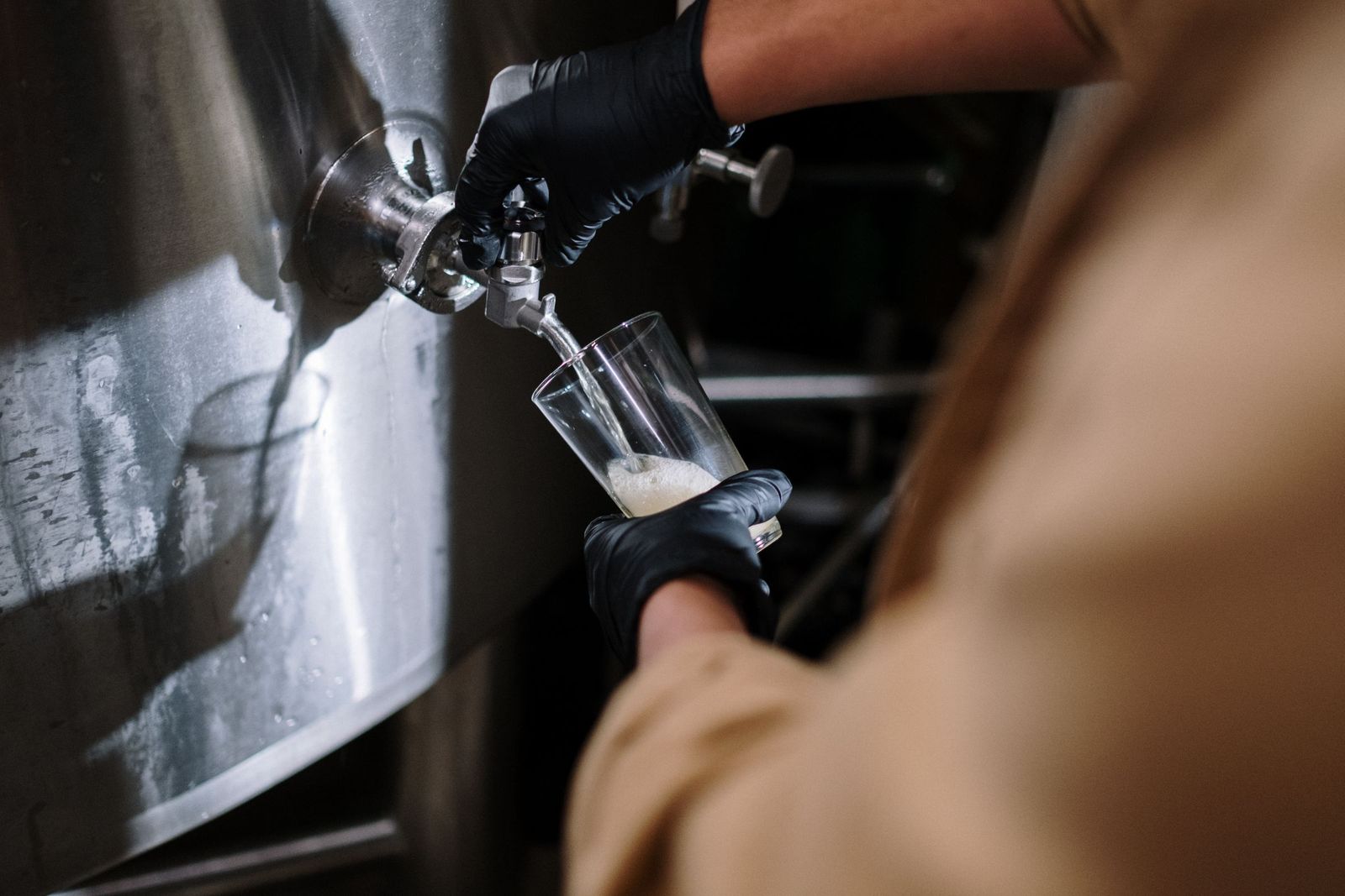 Cervejeiro de luvas enchendo um copo diretamente de um tanque de aço inox